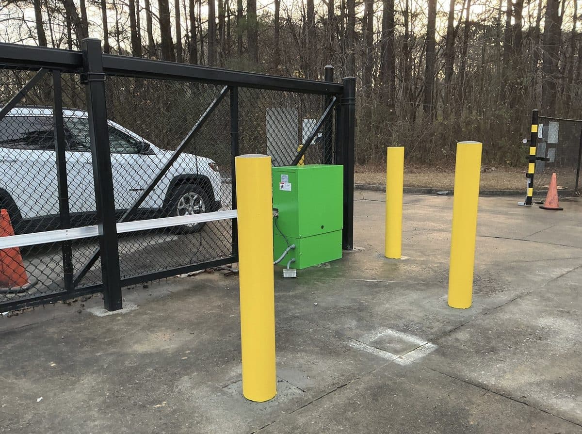 Black chain link gate with operator and yellow bollards in Georgia
